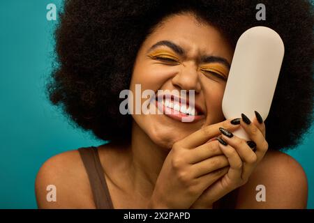 Eine stilvolle afroamerikanische Frau hält vor einem lebendigen Hintergrund einen Pinsel ins Gesicht. Stockfoto