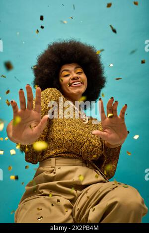 Stilvolle afroamerikanische Frau, die auf dem Boden sitzt, die Hände hoch in der Luft. Stockfoto