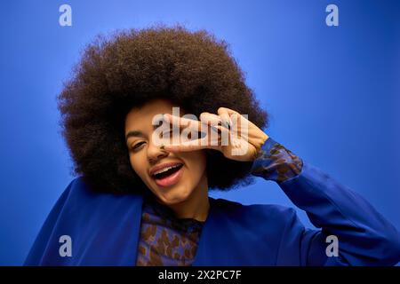 Stilvolle afroamerikanische Frau in trendiger Kleidung, die mit ihren Fingern ein lustiges Gesicht macht. Stockfoto