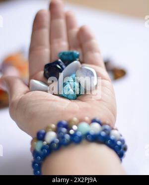 Die junge Frau hält eine Sammlung verschiedener blauer Edelsteine in der Hand, die Heilung, Energie und Wohlbefinden symbolisieren Stockfoto