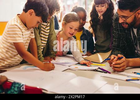 Gruppe von Kindern, die ein Kunstprojekt mit ihrem Lehrer machen. Grundschüler zeichnen gerne mit Malstiften. Kreativität als Teil des Ohr Stockfoto