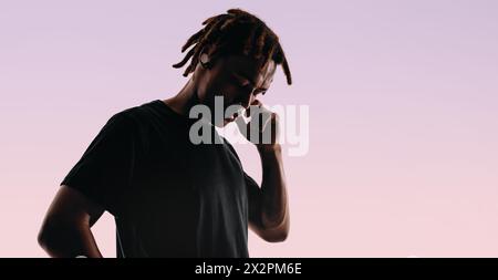 Mann mit Dreadlocks steht in einem Studio vor rosa Hintergrund, die Augen geschlossen in Ruhe. Er hört Musik über schnurlose Ohrhörer, taucht in mich ein Stockfoto