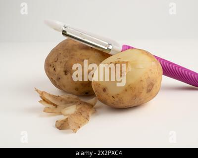 Kartoffelzubereitung mit einem Kartoffelgemüseschäler, isoliert auf weißem Hintergrund Stockfoto