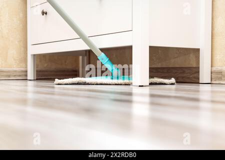 Die Hausfrau wischt den Boden unter dem Schrank. Nassreinigung des Fußbodens im Zimmer. Reinigung von Staub unter Schränken. Stockfoto