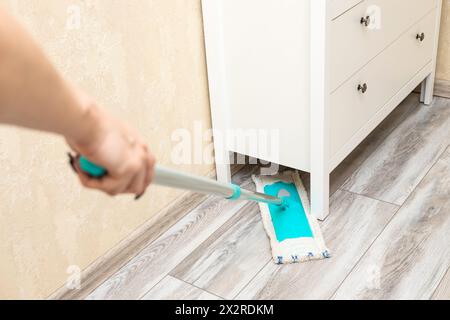 Die Hausfrau wischt den Boden unter dem Schrank. Nassreinigung des Fußbodens im Zimmer. Reinigung von Staub unter Schränken. Hochwertige Fotos Stockfoto