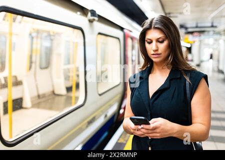 Junge Frau, die ihr Smartphone in der Nähe der U-Bahn am Bahnsteig benutzt Stockfoto