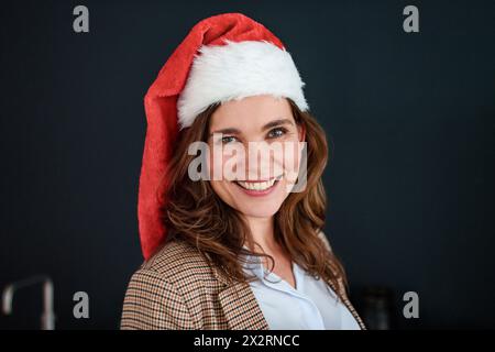 Fröhliche Geschäftsfrau mit weihnachtsmann-Hut vor schwarzem Hintergrund Stockfoto