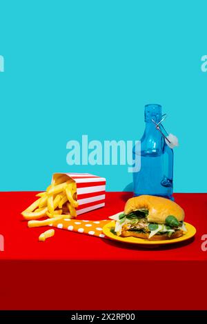 Chicken Burger mit Pommes frites und Limonade-Flasche auf dem Tisch vor blauem Hintergrund Stockfoto