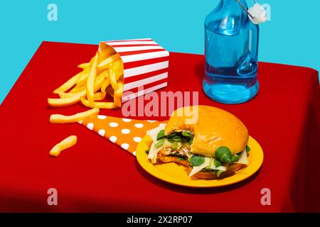 Chicken Burger und Pommes frites mit Limonadenflasche auf dem Tisch vor blauem Hintergrund Stockfoto