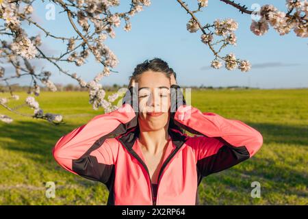 Frau mit geschlossenen Augen in der Nähe von Mandelblüten am sonnigen Tag Stockfoto