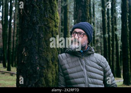 Reifer Mann, der sich im Wald auf den Baumstamm lehnt Stockfoto