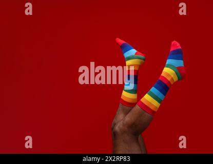 Beine eines Mannes, der bunte Socken vor rotem Hintergrund trägt Stockfoto