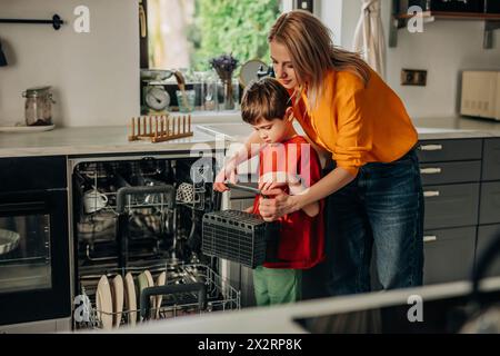 Der Sohn hilft der Mutter beim Waschen von Tellern mit dem Geschirrspüler zu Hause Stockfoto