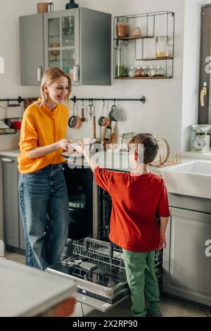 Junge, der Mutter hilft, die Teller zu waschen, indem er zu Hause Geschirrspüler benutzt Stockfoto