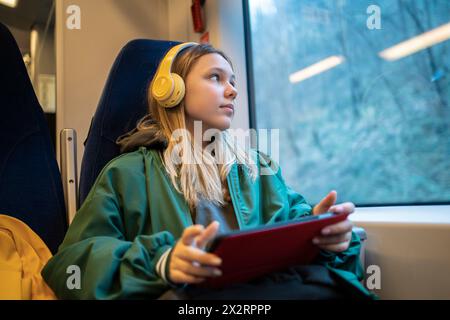 Teenager-Mädchen mit Tablet-PC und kabellosen Kopfhörern im Zug Stockfoto