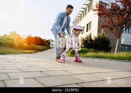 Vater hilft Tochter beim Rollschuhlaufen auf dem Fußweg Stockfoto