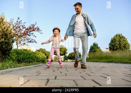 Glückliches Mädchen, das Rollschuhlaufen lernt, mit Vater auf Fußweg Stockfoto