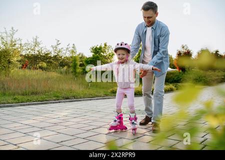 Glückliches Mädchen, das Rollschuhlaufen lernt, mit Vater auf Fußweg Stockfoto