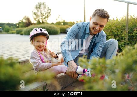 Lächelndes Mädchen mit Vater, der beim Tragen von Rollschuhen im Park hilft Stockfoto