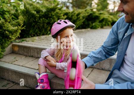 Lächelndes Mädchen in Rollschuhausrüstung, das mit Vater auf Stufen sitzt Stockfoto