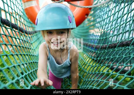 Lächelndes Mädchen, das im Netz im Abenteuerpark krabbelt Stockfoto