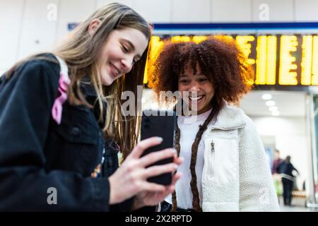 Lächelnde Frau, die dem Freund am Bahnhof das Smartphone zeigt Stockfoto