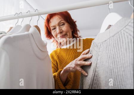 Ältere Frau mit Oberteilen, die im Schrank hängen Stockfoto