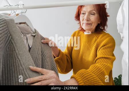 Eine pensionierte Frau, die zu Hause einen Pullover vom Kleiderständer auswählt Stockfoto