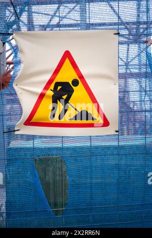 Warnschild für Bauarbeiten an einem Bauzaun mit Materialien und Balken im Hintergrund. Stockfoto