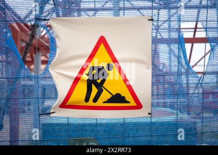 Warnschild für Bauarbeiten an einem Bauzaun mit Materialien und Balken im Hintergrund. Stockfoto