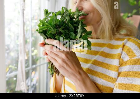 Reife Frau riecht zu Hause nach frischer Minze Stockfoto