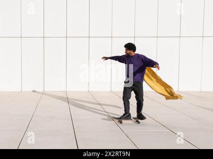 Junger Mann, der vor der weißen Wand Skateboarden trägt Stockfoto