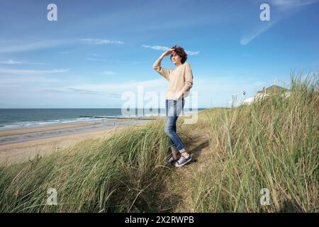 Frau, die Augen abschirmt, steht im grünen Gras am Strand Stockfoto