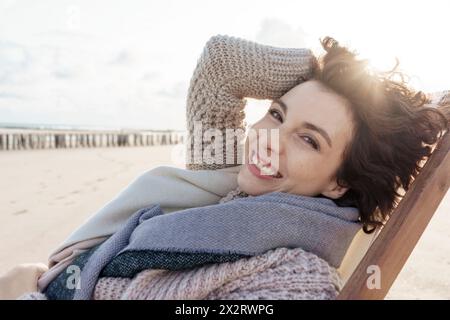 Glückliche Frau, die sich am Strand auf der Liege entspannt Stockfoto