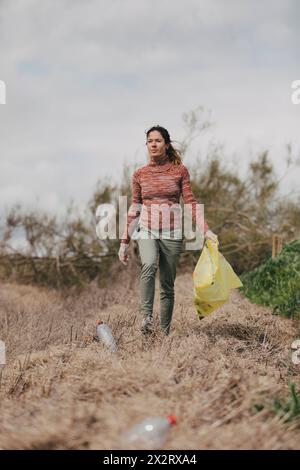 Frau, die Plastiktüte hält und Flaschen auf dem Land sammelt Stockfoto