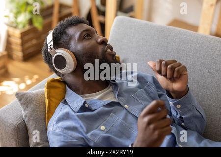 Glückliche, nicht binäre Person, die schnurlose Kopfhörer trägt und zu Hause Musik genießt Stockfoto