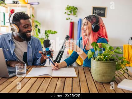 Happy Influencer nehmen Podcast zusammen am Schreibtisch auf Stockfoto