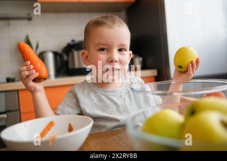 Lächelnder Junge, der Apfel und Karotten in der Küche zu Hause hält Stockfoto