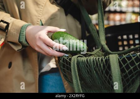 Eine Frau, die Avocado im Supermarkt in einen Netzbeutel steckt Stockfoto