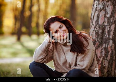 Lächelnde reife Frau, die neben einem Baum im Park sitzt Stockfoto