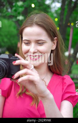 Lächelnde Frau, die Bilder im Park durch die Kamera aufnimmt Stockfoto