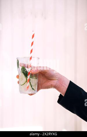 Hand einer Frau, die ein Glas Gurkensaft vor der Wand hält Stockfoto