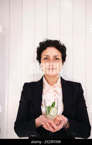 Geschäftsfrau, die ein Glas Gurkensaft vor der Wand hält Stockfoto