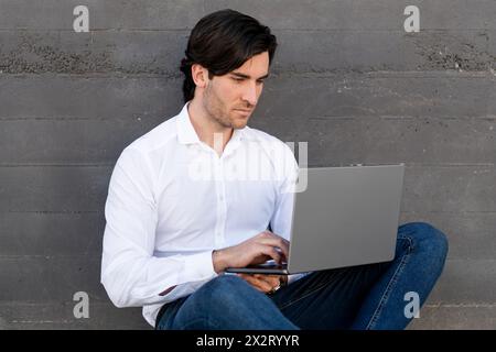 Junger Geschäftsmann mit Laptop vor der Wand Stockfoto