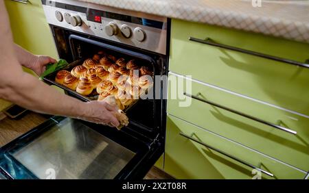 Eine ältere Frau nimmt zu Hause ein Tablett mit süßen Teigbrötchen aus dem Ofen Stockfoto