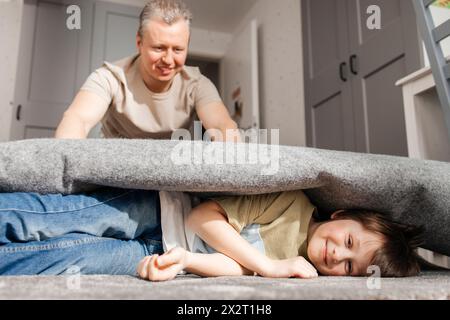 Verspielter Vater rollender Sohn im Teppich zu Hause Stockfoto