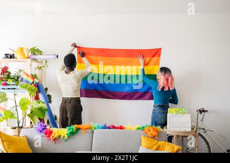 Junge nicht-binäre Person und Freund, die das Haus für eine Homosexuell-Pride-Party dekorieren Stockfoto