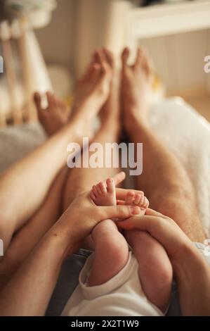 Hände eines Mannes, der die Füße des Babysohnes in der Nähe der Frau zu Hause hält Stockfoto