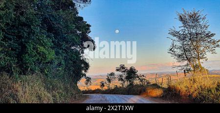 Sonnenuntergang im Inneren von Minas, Landschaft von der unbefestigten Straße aus gesehen, flankiert von grünen Bäumen, ein wunderschöner Horizont mit einem wunderschönen Vollmond im Blau Stockfoto