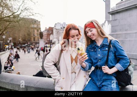 Glückliche Frau mit Freund, die in London ein Smartphone benutzt Stockfoto